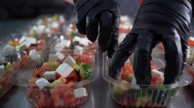 Kauçuk eldivenli eller tek kullanımlık plastik tepsiyi salatayla kapatır. Yemek teslimatı ve paket servis konsepti.