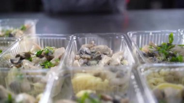 Masada bir sürü plastik tek kullanımlık tepsi var. Şef üstüne maydanoz serper. Yemek teslimatı ve paket servis konsepti.