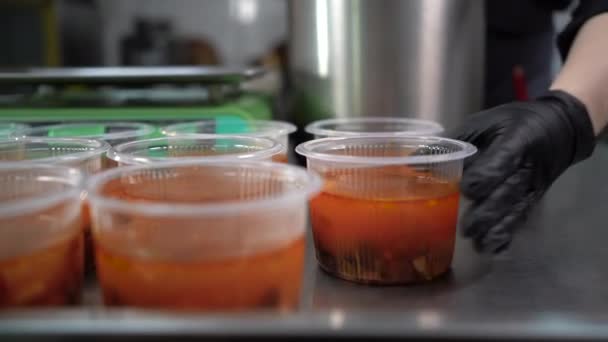 A cup of soup in a disposable plastic container is on the table. The chefs hand in gloves prepares food for delivery. Takeaway food concept. — Stock Video