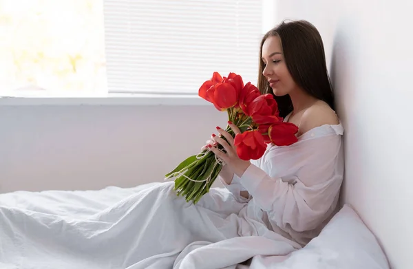 寝室の朝の若い美しい女性はチューリップの大きな花束で座っています 記念日やバレンタインの日などに花を咲かせます スペースのコピー — ストック写真