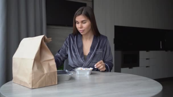 Mujer caucásica por la mañana en casa se sienta a la mesa abre una bandeja desechable hecha de papel de aluminio y comienza a desayunar. Entrega de alimentos ordenar el desayuno en línea. — Vídeos de Stock