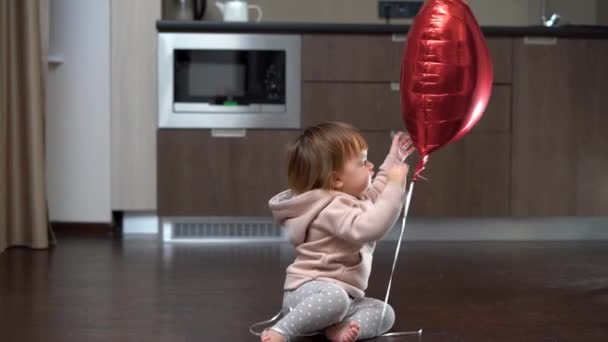 Kid sitting on the floor with a big balloon heart, child on Valentines Day, toodler playing with foil balloon alone, happy childhood concept — 图库视频影像