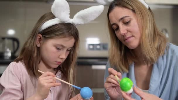 Wielkanoc. Close-up portret mama i córka z zajęczymi uszami przygotowują się do wakacji, malować jajka w przytulnej kuchni w domu siedzi przy stole. dobrze się komunikować i spędzać razem czas. — Wideo stockowe