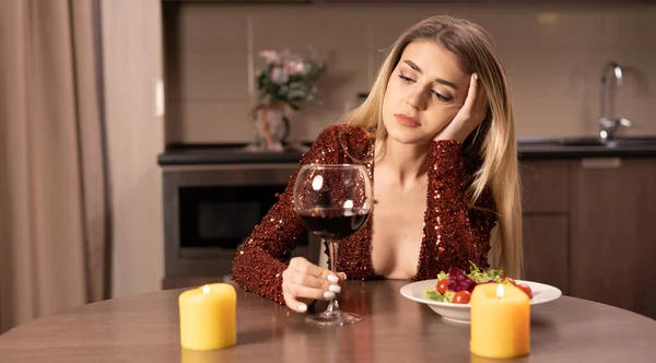 赤いドレスを着た美しい女性がワインを片手にテーブルに座り 悲しい表情で頭を下げた このコンセプトはバレンタインデーや記念日に孤独です コピースペース ウェブカメラの眺め — ストック写真
