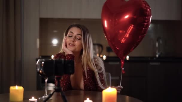 Mladý pár mluví a posílají lásku k sobě na virtuální rande na Valentýna. Šťastná žena vesele chatuje na video komunikaci a drží srdce ve tvaru balónu. — Stock video