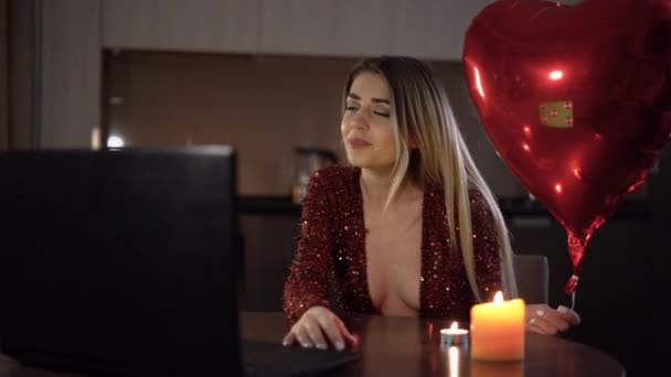 バレンタインデーのビデオ通話。夜の女性は仮想の日付にハート型の風船でノートパソコンの近くに座っています。バレンタインデーまたは記念日のコンセプト. — ストック動画
