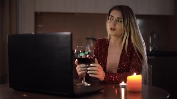 Videohívás Valentin napon. A virtuális dátum, egy nő ül otthon a konyhában este kezében egy pohár vörösbor a kezében, és élvezi a kommunikációt közben egy video chat egy szeretett — Stock videók