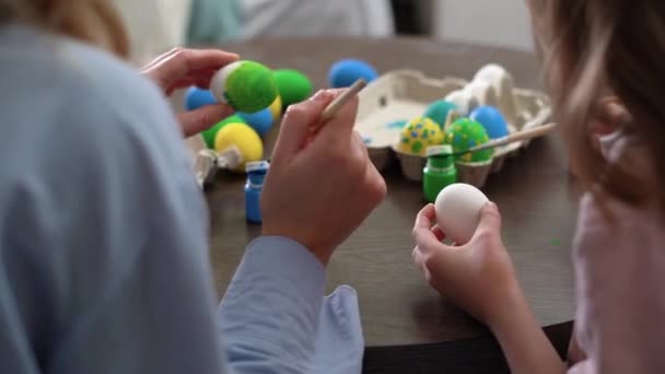 Easter. Close-up mom and daughter are preparing for the holiday, painting eggs in a cozy kitchen at home, sitting at the table. communicate nicely and spend time together. without a face. — Video Stock