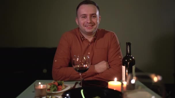 First person portrait of Caucasian man. boyfriend sits at the table in the evening with a glass of wine during a date for an anniversary or Valentines Day. romantic dinner for two. — Wideo stockowe