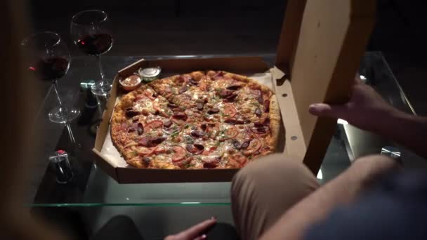 Top view of fresh pizza on the table in a box near two glasses of wine. Male hands open the box. — Vídeo de Stock