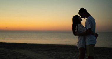 Two young lovers stand on the beach and look at each other against the backdrop of the sunset. Summer vacation concept while vacationing on a tropical beach. Baner. Copy space.