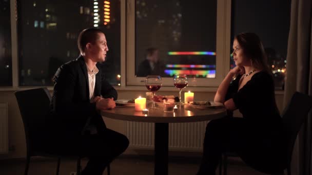 . Beautiful young couple in love sitting at the table at home. Smiling man communicates with his woman. Glasses with wine and candles on the table. Celebrating valentines day or anniversary. — Wideo stockowe