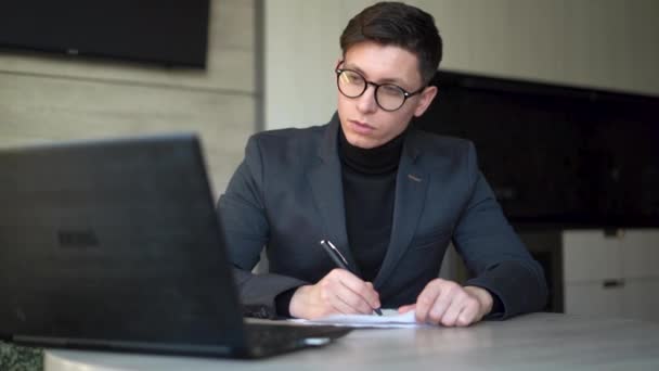 Νεαρός άνδρας, επιχειρηματίας με γυαλιά, κάθεται στο χώρο εργασίας στο γραφείο στο σπίτι με φορητό υπολογιστή, online εργασία και εκπαίδευση, πωλήσεις ηλεκτρονικού καταστήματος, ζουμ επικοινωνίας βίντεο. — Αρχείο Βίντεο