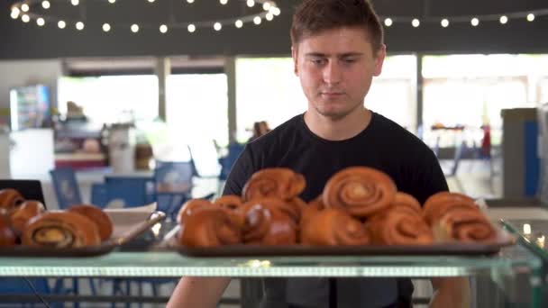 There are cinnamon rolls on the display at the bakery, a Caucasian male shopper picks out a dessert and grabs one roll. — Video