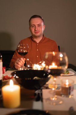 Date or valentine's day online. Man with glass of wine at dinner table smiling at webcam. romantic dinner remotely. Concept for celebrating valentine's day or holiday online