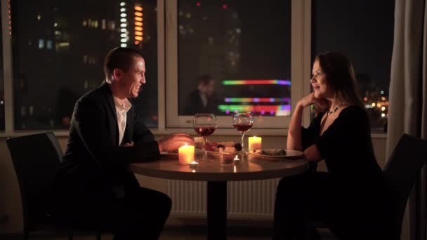 Romantic dinner at home for two. A couple in love sits at a table, a man says a toast and raises a glass. concept for celebrating valentines day or anniversary. Red wine and candles on the table. — Video Stock