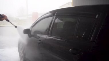 a man washes a car using a pressure washer on the street.
