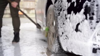 A man washes a black car. clean rims and wheels with a wheel brush in a self-service car wash. Car service industry.