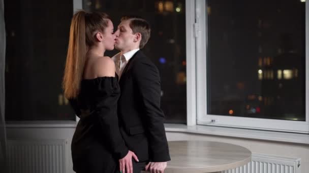 Couple in love man and woman stand at night near a large window and kiss on the background of the night city. Lovers in the hotel rooms. — Stockvideo
