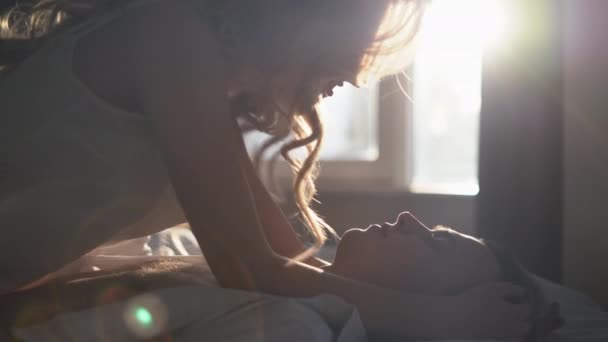 Joven pareja feliz acostados juntos en la cama besándose por la mañana al amanecer en una habitación de hotel. una mañana sin preocupaciones para los amantes. Día de San Valentín — Vídeos de Stock