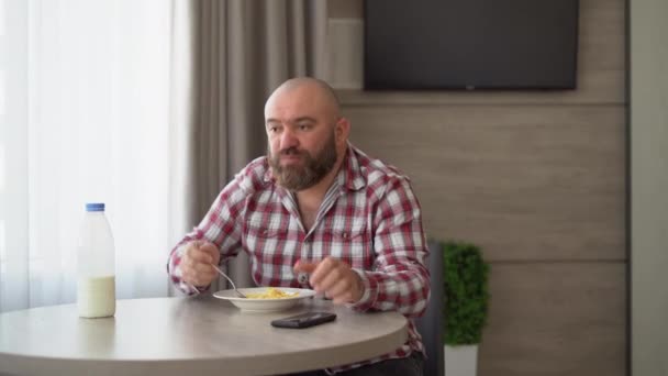 Man is having breakfast of cornflakes with milk, using a mobile phone, reads the news online. — Stock Video