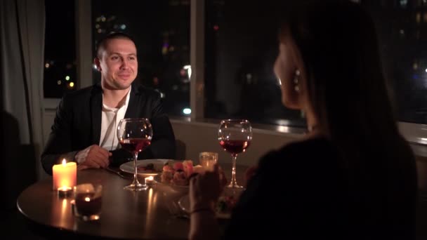家庭でのロマンチックなキャンドルライトディナー。夜の街を背景に男と女がテーブルに座り、コミュニケーションをとる。バレンタインデー、記念日、記念日のお祝いのコンセプト — ストック動画