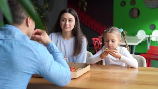 The family spends time together, mom with dad and daughter are sitting at the table and eating pizza. — Vídeo de Stock