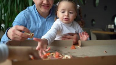 The girl sits in the mans arms and eats delicious pizza. Father and daughter spend time together. Fathers day concept.