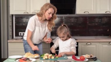 Mom teaches daughter to cook sandwiches for breakfast, bread with salmon and vegetables, cooking sandwich in the kitchen
