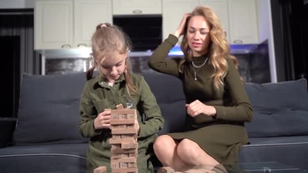 Family plays jenga sitting in the living room by the window. Woman and child spend time together. — Vídeo de stock