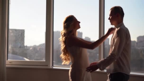 A young couple hugging and kissing near a large window overlooking the city. Lovers or spouses have a good and carefree time together. — Vídeo de Stock