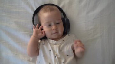 little boy 6 months old lies on the bed in headphones and listens to music, space for text, top view.