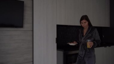 Young happy cheerful housewife dressed in casual clothes eats pancakes and citrus fresh juice for breakfast, cooks food in the light kitchen at home alone Healthy food and lifestyle concept.