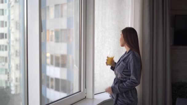 People and vacation concept happy caucasian woman drinking citrus juice or smoothie at home standing near window in casual clothes in morning. — стоковое видео