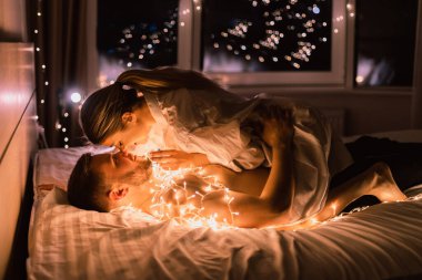 Beyaz adam ve kadın, gece çelenklerin ışığında yatağa uzanıyorlar. Aşık bir çiftin evindeki romantik randevu kavramı..