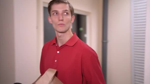 Un messager qui livre de la nourriture à emporter se promène le long du couloir d'un immeuble résidentiel à plusieurs étages et cherche un numéro d'appartement. Service de livraison. — Video