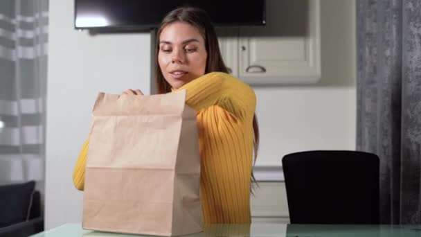 Ung flicka med hämtmat hemma i köket. Kontaktlös leverans. Hantverksförpackning med livsmedelsbehållare, ger lunchleverans — Stockvideo