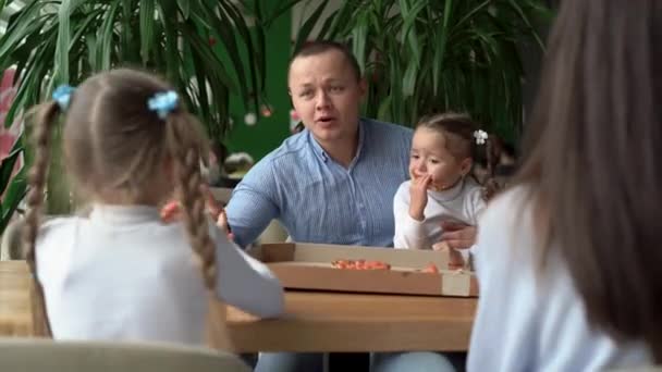Сімейний обід з дітьми піца в ресторані, тато, мама і дві дочки їдять італійську піцу в кафе, фаст-фуд для дітей, концепція ресторанного харчування — стокове відео