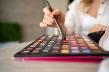 Bir makyöz yeni göz farı paleti hakkında konuşur ve yeni çevrimiçi video kursu için nasıl makyaj yapılacağını açıklar. Makyaj fırçası yakın plan renkli palet