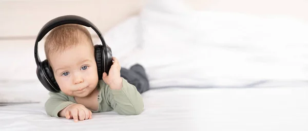 ヘッドフォンで音楽を聞いて白い背景にかわいい赤ちゃん 赤ちゃん3ヶ月イヤホンでベッドの上に横たわって 幸せな屈託のない子供時代のコンセプト バナー テキストのための場所 — ストック写真