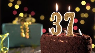 37 numaralı mumlu doğum günü pastası. Parlak bir arka planda yanıp sönen ışıklar. Çakmağın ateşi..