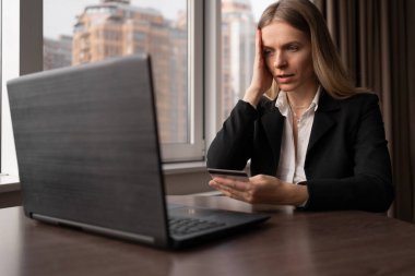 İnternetten alışveriş konsepti. Ofiste kredi kartı ve dizüstü bilgisayarı olan üzgün bir kadın, online alışveriş ve finansal dolandırıcılık, kartıyla sipariş ve ödeme, fotokopi alanı