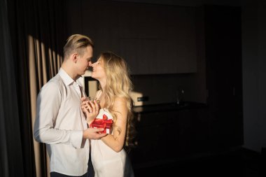 Sevgililer Günü 'nü ya da evlilik yıldönümünü kutlayan genç bir çift. Mutlu bir adam bir kadına sabah güneşinde kırmızı bir kutu verir. Boşluğu kopyala.