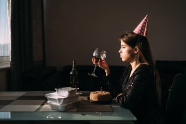 Yalnız bir doğum günü, masada oturan bir kız bardakta şarap içer, izole bir tatil, evde tatil yapma kavramı.