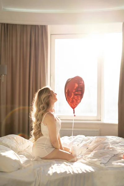 バレンタインデー 女性の日 記念日や記念日 女性がベッドに座り 2月14日に赤いハート型の箔風船でお祝いします コピースペース — ストック写真