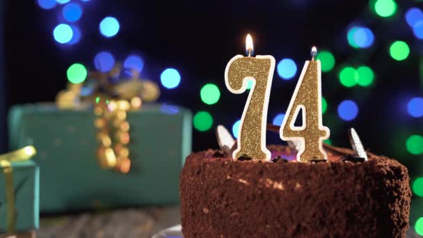 Número setenta e quatro vela de aniversário em um bolo doce na mesa, 74 anos. Fogo do isqueiro, apaga a vela do feriado. — Vídeo de Stock