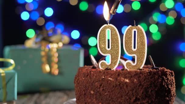 Lilin ulang tahun nomor sembilan puluh sembilan di atas kue manis di atas meja, ulang tahun ke-99. Api dari korek api, meniup lilin liburan. — Stok Video