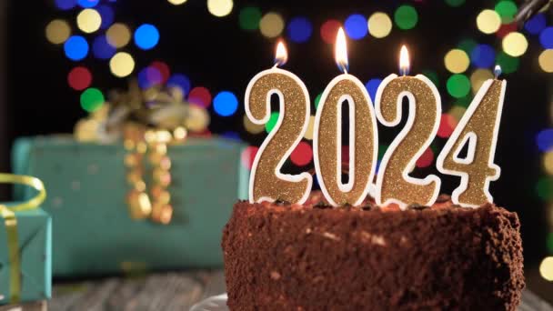 Feliz Año Nuevo. vela dorada número dos mil veinticuatro en un pastel dulce en la mesa, 2024. Fuego de un encendedor, apague la vela festiva. — Vídeo de stock