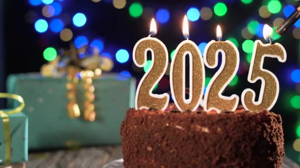 Frohes neues Jahr. Goldene Kerze Nummer zweitausendfünfundzwanzig auf einem süßen Kuchen auf dem Tisch, 2025. Feuer aus einem Feuerzeug, blasen Sie die Festkerze aus. — Stockvideo