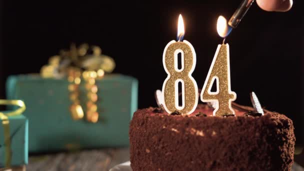 Номер восемьдесят четыре свеча на сладком торте на столе, 84-й день рождения. Огонь из зажигалки, задуть праздничную свечу. — стоковое видео